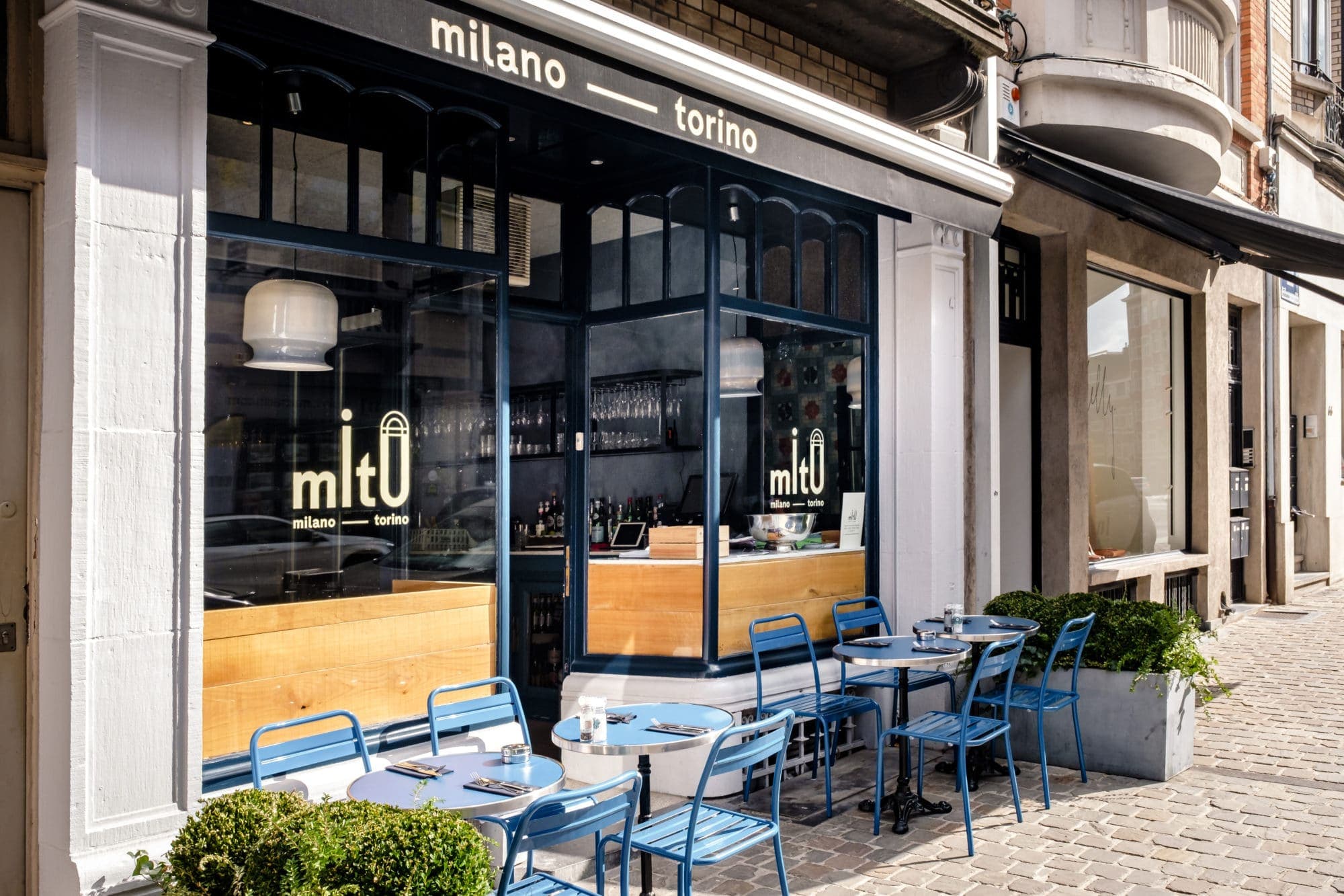 La devanture bleu nuit de MiTo Brugmann rue Darwin, avec ses tables et chaises bleues en terrasse